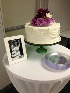 a white cake with purple flowers sitting on top of a table next to a photo