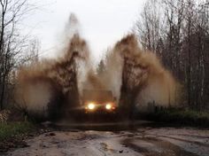 a truck is driving down a muddy road with trees in the background and dust coming from its tires