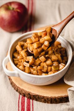 a wooden spoon full of food sitting on top of a table next to an apple