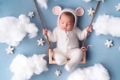 a baby is sleeping on a swing with clouds and stars in the sky behind it