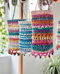 multicolored crocheted baskets hanging from hooks in front of a potted plant