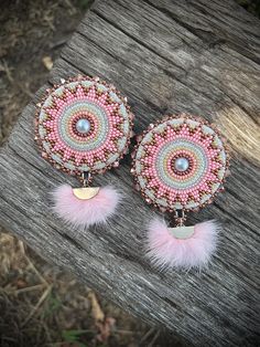 the pink earrings are decorated with beads and feathers on top of wooden planks in front of grass