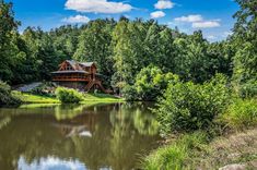 a large house sitting on top of a lush green hillside next to a lake and forest