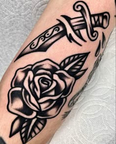 a black and white rose with two swords on its arm, tattoo artist's work