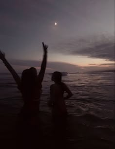 two women are standing in the water with their arms up and one is holding her hand up