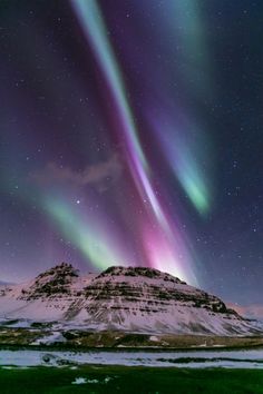 the aurora lights shine brightly in the night sky over snow covered mountains and green grass