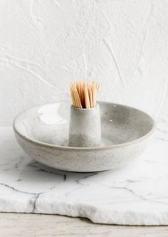 two toothbrushes in a white bowl on a marble counter