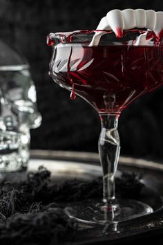 a glass filled with red liquid sitting on top of a table next to two skulls