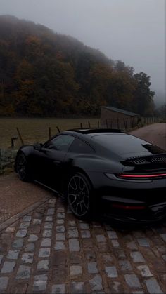 a black sports car parked on the side of a road in front of a foggy mountain