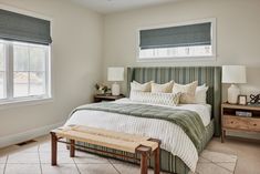 a bedroom with a large bed, two windows and a bench in front of it