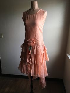 "1920s peach gauze drop waist tea dress sleeveless scoop neck high tie back ruffle tier skirt back 2 ruffle tiers are longer then rest of hem 6 side snap buttons from drop waist up w/hook eyes at bottom (waist side)/top(underarm) decorative horizontal seam lines down front chest decorative low center flower w/ribbon unlined hand made no tags feels like acetate or some other synthetic very good vintage condition, light wear no tags measures, lying flat, shoulder-12\" bust-16\" waist-14 1/2\" drop Sleeveless Ruffled Dress For Vintage Events, 1920s Style Dresses For Vintage Summer Events, 1920s Style Summer Dresses For Vintage Events, Vintage Apricot Dress For Spring, 1920s Style Day Dresses For Spring, Fitted 1920s Style Summer Dresses, Sleeveless Dresses For Vintage Summer Events, Summer Flapper Style Fitted Dress, Sleeveless Summer Dresses For Vintage Events