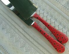 two red handled knives sitting next to each other on top of a white tablecloth