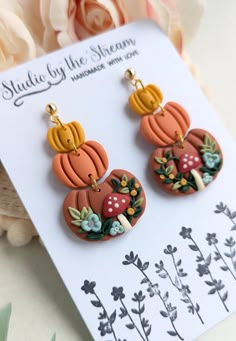 the earrings are decorated with flowers and pumpkins on them, sitting next to a card