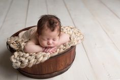 a baby sleeping in a wooden bucket on a white wood floor with his hands under his chin