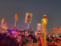 a large group of people standing around each other at a music festival in the evening