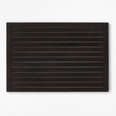 a black wooden slatted surface mounted on a wall with white walls behind it