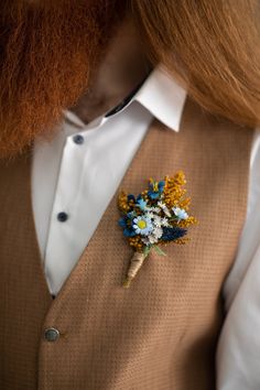 a man with long red hair wearing a vest and flower brooch on his lapel