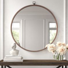 a round mirror sitting on top of a wooden table next to a vase with flowers