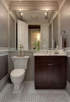 a white toilet sitting next to a sink in a bathroom under a mirror and lights