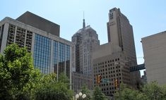 the city is full of tall buildings and green trees in the foreground, with traffic lights on either side