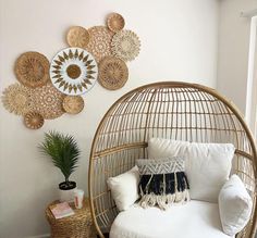 a wicker swing chair with white pillows and decorative plates on the wall