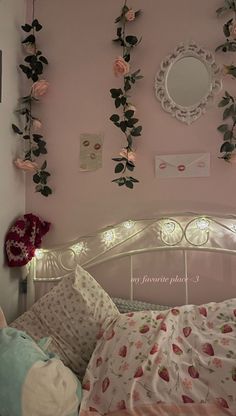 a bedroom with pink walls and flowers hanging on the wall above the bed, along with an illuminated mirror