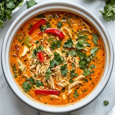 a white bowl filled with soup and garnished with cilantro, red peppers, parsley