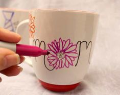 a person is writing on a coffee cup with a pink pen in their left hand