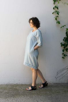 a woman standing in front of a white wall with her hands on her hips, wearing sandals and a striped dress