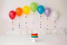 a cake with rainbow frosting and balloons on the wall behind it in front of a white backdrop