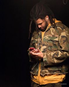 a man with dreadlocks is looking at his cell phone while standing in the dark