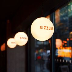 three lights hanging from the ceiling in front of a window with sizzles written on them