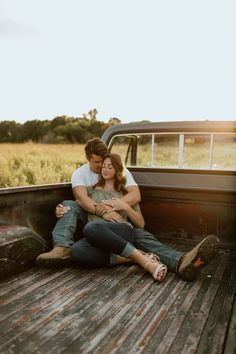 a man and woman sitting in the back of a pick up truck with their arms around each other