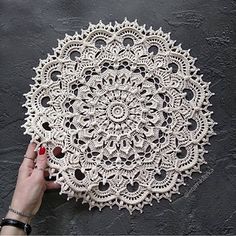 a hand holding an ornate doily on a black surface with grey walls in the background