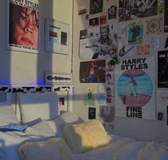 a bedroom with posters on the wall and a bed covered in white sheets, pillows and blankets