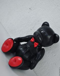 a black teddy bear with a red bow on it's neck sitting on the floor