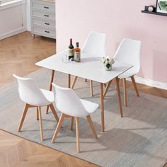 a white dining table with four chairs in front of it on a rug next to a pink wall