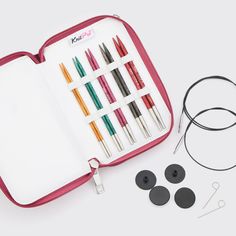 an open case with several pens and earphones in it next to other items on a white surface