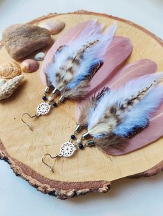 two pairs of feather earrings on a piece of wood next to shells and seashells