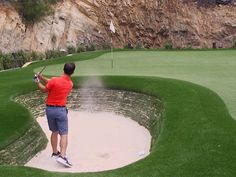 a man in red shirt playing golf on green field with water spewing out from hole