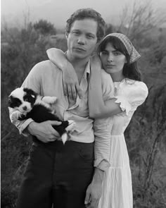 a man and woman are holding a small dog in their arms as they pose for a black and white photo