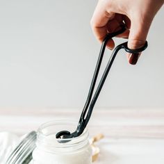 a hand holding a spoon over a jar filled with whipped cream and black plastic utensils