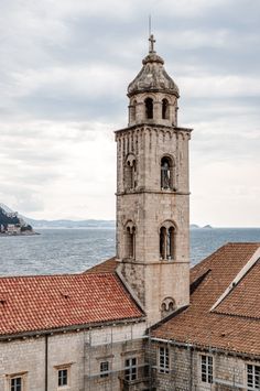 an old building with a steeple next to the ocean and mountains in the background