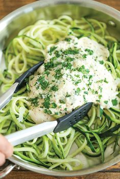 someone is holding two tongs over some green noodles in a pan with sauce and parmesan cheese on top