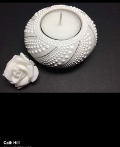 a white candle sitting on top of a table next to a small white rose flower