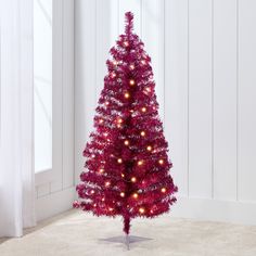 a red christmas tree with lights on it in a room next to a white wall