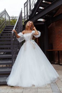 a woman in a white wedding dress is standing on some stairs and posing for the camera