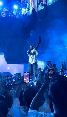 a man standing on top of a stage surrounded by people holding up cell phones in the air