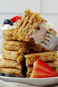 a stack of pancakes with strawberries and whipped cream on top, being held by a fork