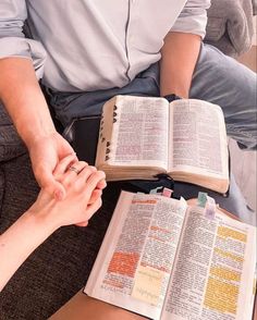 two people sitting on a couch holding hands with an open book in front of them